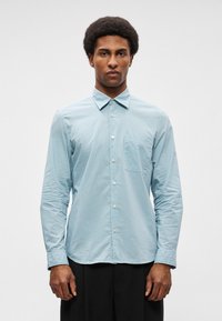 Ανοιχτό μπλε πουκάμισο με γκέσο μοτίβο, μακριά μανίκια, τσέπη στο στήθος και μεταλλικά κουμπιά. Λείο υφάδι, ραμμένο εφαρμοστό.