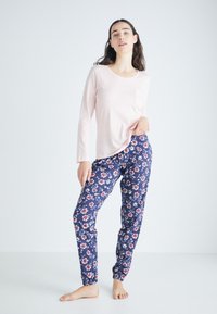 Ljusrosa långärmad topp med en ficka, i kombination med marinblå blommönstrade pyjamasbyxor med elastisk midja och manschetter vid anklarna.