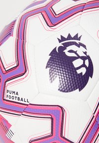 Puma fodbold med en hvid overflade, hexagonale paneler, lilla og lyserøde geometriske linjer, samt et fremtrædende mørkeblåt løve-logo.