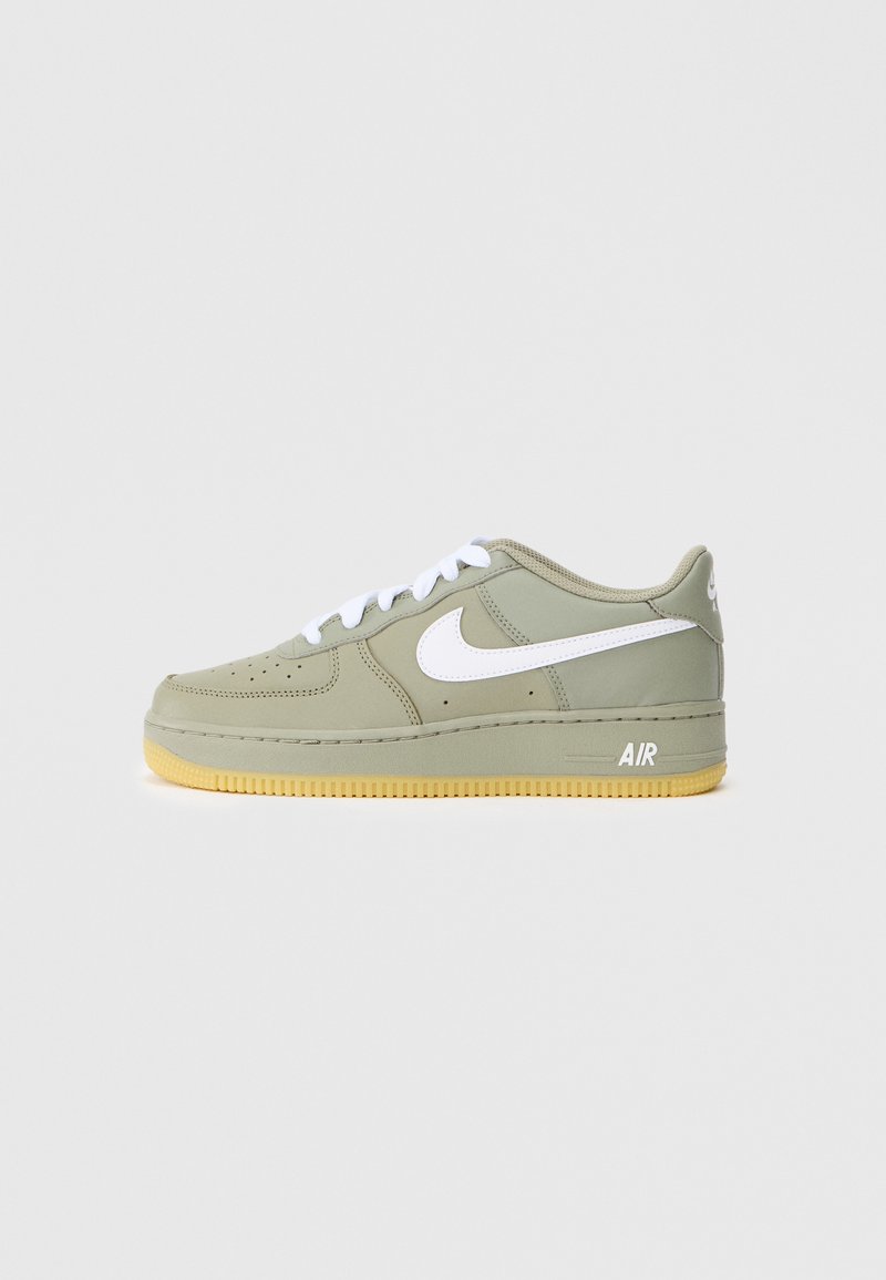 Jasnozielone sneakersy Nike Air Force 1 z białymi akcentami, okrągłym noskiem, perforowanym wzorem i żółtą gumową podeszwą. Standardowe zapięcie na sznurówki.