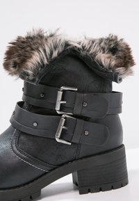 Černé kožené kotníkové boty s límcem z umělé kožešiny, dvěma kovovými sponami, texturovanou gumovou podrážkou a masivním podpatkem.