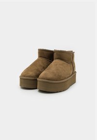 Botas de ante marrón hasta el tobillo con un diseño de punta redonda, que presentan una suela de plataforma gruesa y texturizada y costuras en contraste a lo largo de las costuras.
