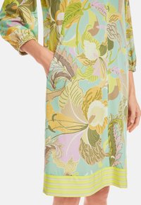 Blumenkleid mit mintgrünem Grundton, großen, mehrfarbigen Blumenmustern, elastischen Ärmelbündchen und einem gestreiften Saum in Grün und Gelb.