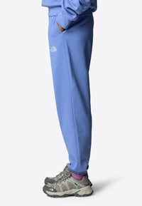 Helle blaue Sweatpants mit lockerer Passform und Seitentaschen, kombiniert mit robusten grauen Wanderschuhen, wobei lila Socken sichtbar darüber hervorblitzen.