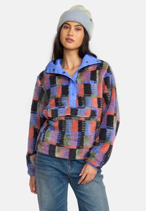 Fleece pullover met een meerkleurig geruit patroon, voorzien van een blauwe ritskraag en zachte, gestructureerde stof. Gecombineerd met een gestreepte muts.
