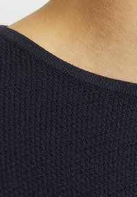Tejido de punto texturizado en un azul marino oscuro con un escote redondeado y suave, mostrando los finos detalles del patrón de punto y el tono de piel que hay debajo.