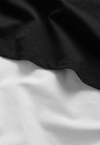 Schwarzer und weißer Baumwollstoff, die übereinander geschichtet sind und eine weiche Textur sowie geschwungene Kanten zeigen. Der schwarze Stoff überlappt den weißen Stoff an der Naht.