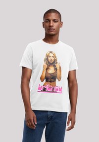 Weißes Baumwoll-T-Shirt mit einem bunten Grafikdruck einer Frau mit langen Haaren, die ein braunes Oberteil trägt, und dem Text "britney" in Pink am unteren Rand.