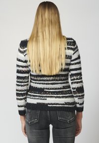 Knitted sweater with black, white, and colorful striped patterns. Features long sleeves, textured fabric, and fitted design.