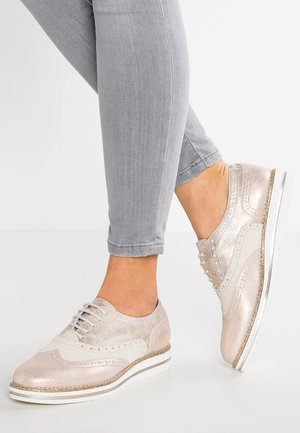Chaussures Oxford en cuir métallisé rose clair avec des accents en cuir blanc, présentant un motif brogue, des surfaces texturées et une semelle blanche épaisse.