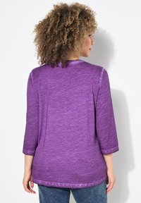 Lila tröja med trekvartsärmar och en strukturerad, melerad mönster. Mjuk tyg med rundad halsringning och avskalad fåll.