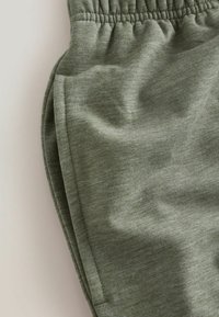 Zbliżenie zielonych oliwkowych spodni dresowych pokazujące elastyczny pas i przeszycia kieszeni bocznej na miękkim materiale.