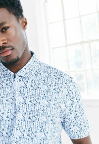 Koszula z krótkim rękawem, z kołnierzykiem, wykonana z lekkiego materiału, z niebiesko-białym wzorem przedstawiającym różne obiekty. Zamek błyskawiczny z przodu.