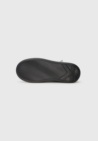 Black rubber sole of a shoe with wave-like traction pattern and a large "K" design near the heel area.