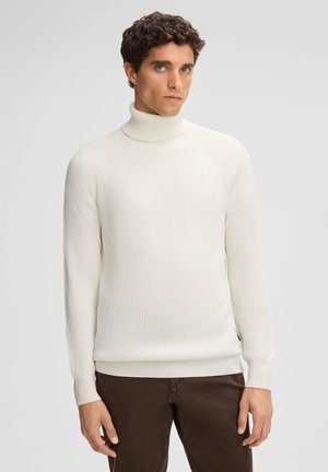 Weißer gerippter Rollkragenpullover mit langen Ärmeln und figurbetontem Schnitt. Kombiniert mit braunen Hosen, zeichnet sich durch eine dezente Textur und seitliche Details aus.