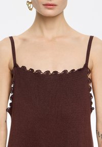 Top marrone senza maniche con una finitura texturizzata, caratterizzato da un delicato profilo in pizzo lungo il collo e i giromaniche, che mostra intricati dettagli a scallop.