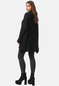 Maglione oversized nero a maglia con maniche lunghe, caratterizzato da una vestibilità ampia e orlo asimmetrico, abbinato a jeans skinny scuri e stivali platform neri.