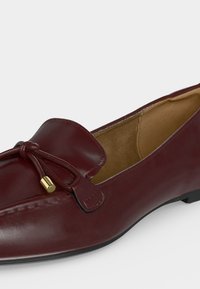 Mocassin en cuir rouge foncé avec bout arrondi, nœud décoratif avec embouts en métal doré et doublure intérieure beige clair.