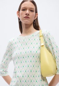 Λευκό ριγωτό πουκάμισο με σχέδια καρδιάς σε μπλε και πράσινο χρώμα, συνδυασμένο με κίτρινη καμπυλωτή τσάντα χειρός με λεία υφή και χρυσά διακοσμητικά.