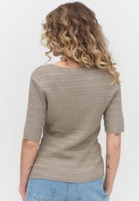 Beige neulepaita lyhyillä hihoilla, jossa on vaakasuoria raitoja ja pyöreä kaula-aukko. Kankaassa on teksturoitu kuvio, jossa on pieniä aukkoja.