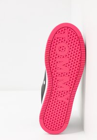 Černý spodní část tenisky s jasně růžovou gumovou podrážkou, která má texturovaný vzor a embosované logo "TOMMY".