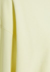 Tissu jaune clair avec une texture douce. Présente une surface lisse et tombe délicatement, avec une couture visible le long du bord.