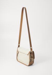 Sac à épaule en toile beige avec des accents en cuir synthétique marron, fermeture zippée en haut et bandoulière réglable. Présente des éléments en métal et des détails de couture.
