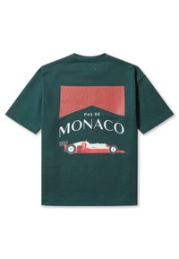 Roheline T-särk, millel on punane ja valge graafika, mis kujutab võidusõiduautot ja punased triibud, tagaküljel on tekst "PAS DE MONACO".