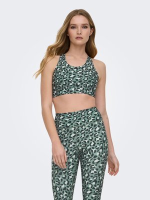 Jeune femme portant un brassière de sport à motif animalier vert et noir et un legging taille haute assorti, debout devant un fond uni.