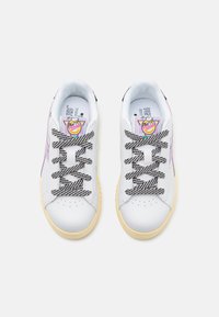 Weiße Sneakers mit einem glatten Lederobermaterial, schwarz-weißen Schnürsenkeln und einer gelben Gummisohle. Mit einem bunten Grafikum auf der Zunge.
