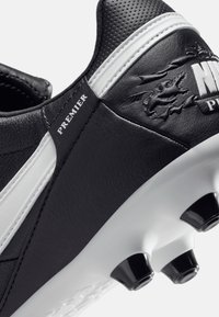 Botte de football noir et blanc avec une tige en cuir synthétique, des accents texturés, un logo Nike surdimensionné et des crampons noirs sur une semelle blanche.