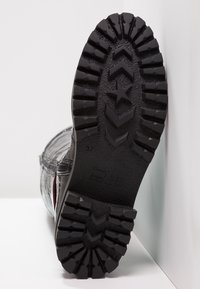 Czarna gumowa podeszwa buta z głębokim bieżnikiem, ozdobiona wzorem gwiazdy i logo. Wierzch ma wzorzysty fakturę i kontrastujące czerwone akcenty.