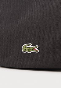 Black fabric bag featuring a green and white embroidered crocodile logo, displaying detailed stitching and a smooth texture.