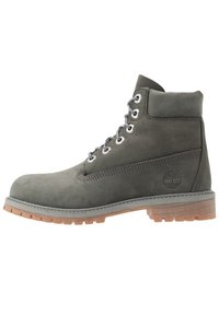 Šedé semišové kotníkové boty s kulatou špičkou, kovovými očky a šedými tkaničkami. Mají strukturální gumovou podrážku s přirozeným vzhledem dřeva.