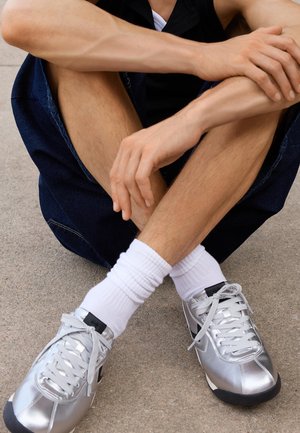 Scarpe sportive argento con una finitura liscia, dettagli neri e lacci grigi. Indossate con calze bianche a costine e pantaloni shorts in denim.
