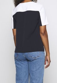 Top a maniche corte color block blu navy e bianco con chiusura a cerniera sul retro, realizzato in tessuto morbido, presenta linee semplici e una vestibilità rilassata.