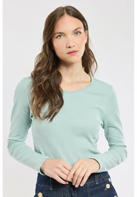 Haut long à manches en teal clair avec un col rond. Texture douce et coupe ajustée. Assorti à un pantalon en denim foncé taille haute.