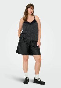 Top sin mangas negro con encaje, con un patrón geométrico, combinado con pantalones cortos de cuero sintético negro de cintura alta y zapatos gruesos negros.