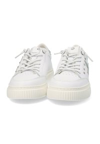 Zapatillas blancas de cuero con puntera redondeada, suela de goma texturizada, detalles en cordones plateados y pequeñas adornos metálicos en la parte superior.