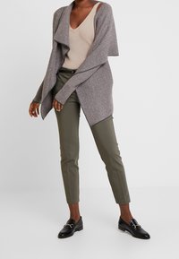 Pletený kardigan v šedém herringbone vzoru, vrstvený přes béžové tílko. Spárovaný s olivově zelenými zúženými kalhotami a černými mokasíny.