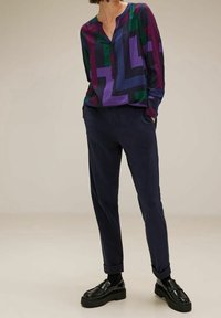 Flerfärgad blus med mönster och djup halsringning; mörka byxor med skräddarsydd passform och uppvikta fållar; svarta platåskor.