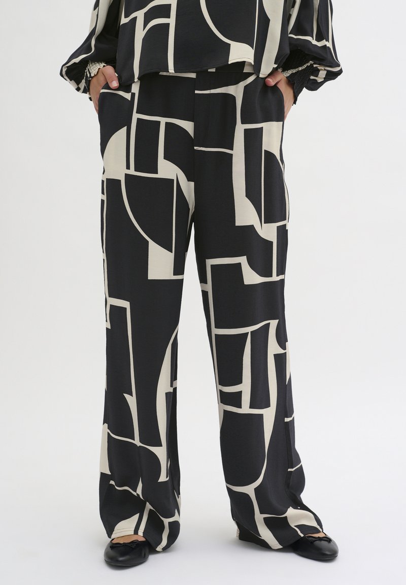 Black and cream patterned wide-leg trousers made of a soft fabric, featuring geometric shapes and a relaxed fit. Black flats complete the look.