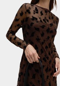 Hnědé průsvitné šaty s dlouhými rukávy, zdobené černou květinovou výšivkou. Hladký povrch, přiléhavý střih, doplněné černou kabelkou.