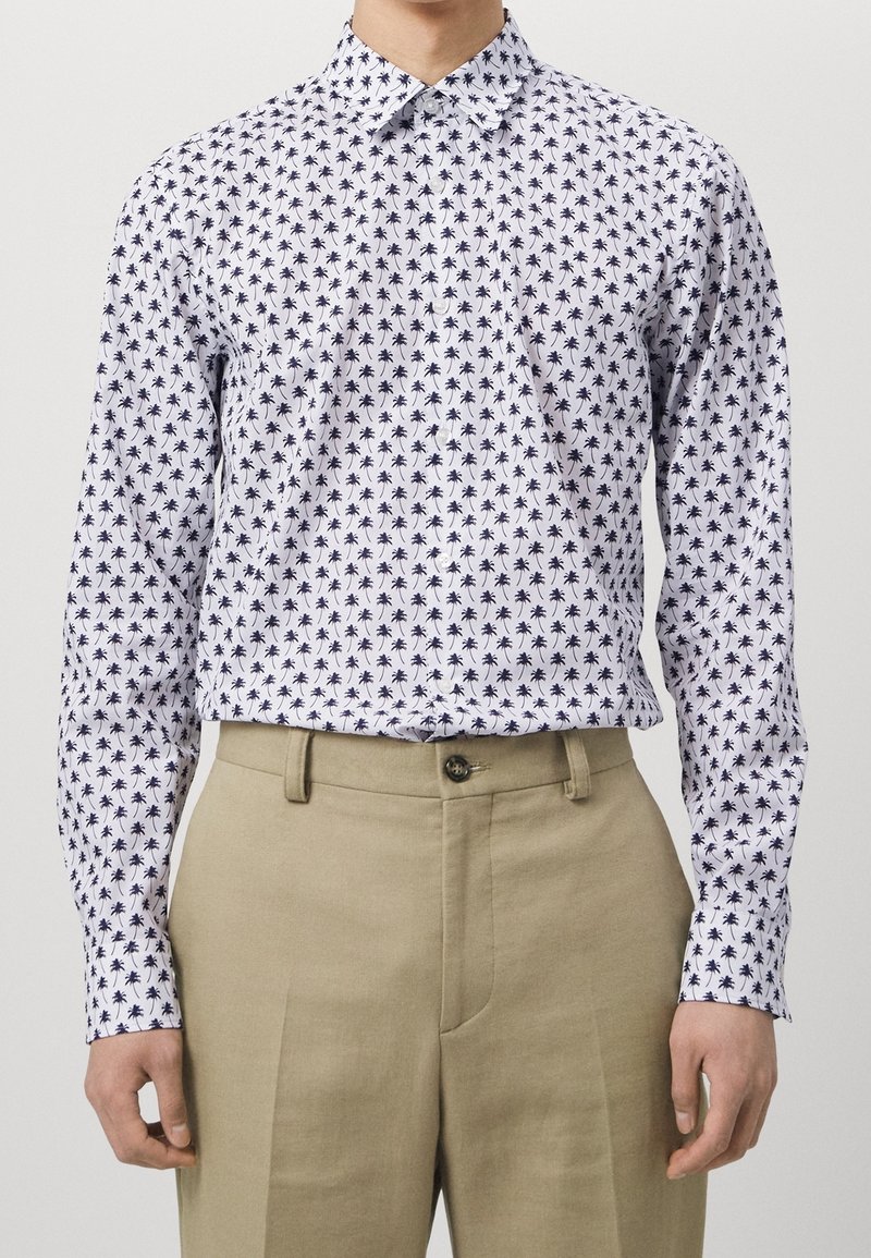 Witte langekleurige shirt met een marineblauw palmbompatroon, met een knoopkraag en manchetten, gecombineerd met beige broeken. Glad katoen stof.