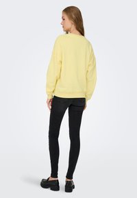 Sweatshirt galben supradimensionat cu umeri căzuți, mansete și tiv cuari, asortat cu blugi negri skinny și încălțăminte chunky neagră.