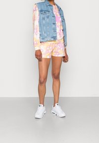 Veste en denim avec deux poches poitrine, sweat à capuche rose et jaune à motif floral, shorts assortis et baskets blanches.