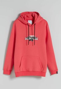 Korallfärgad sweatshirt med huva, framficka, svarta snören och ett grafiskt tryck med text och en illustration på bröstet.
