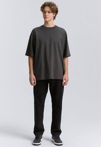 Perdidelio tamsiai pilkos spalvos marškinėliai su trumpomis rankovėmis ir apvalia iškirpte. Derinami su juodomis kelnėmis ir tamsiais batais, fone neutrali spalva.