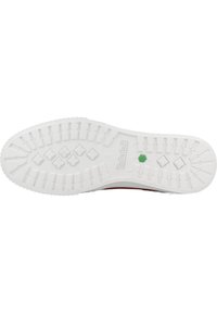 Suela de zapato de goma en blanco con patrón de agarre texturizado, que presenta un punto verde y el logo "Timberland" en relieve cerca del talón.