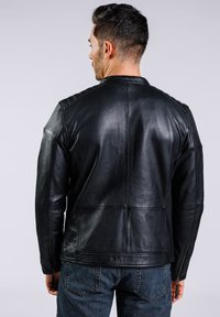 Chaqueta de cuero negro con hombros estructurados y puños con cremallera. Presenta una textura suave y detalles de costura, adecuada para uso casual.